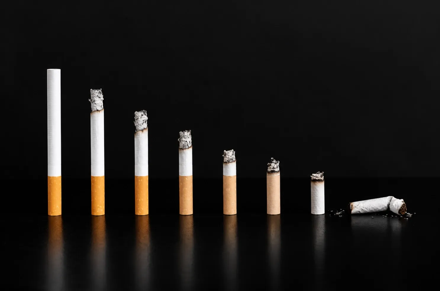 Fila de cigarrillos sobre fondo negro, cada uno más consumido que el anterior, hasta terminar en una colilla rota