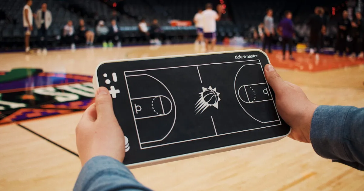 Manos sosteniendo una tableta háptica de Ticketmaster con la cancha de los Phoenix Suns en relieve, en el estadio antes de un partido
